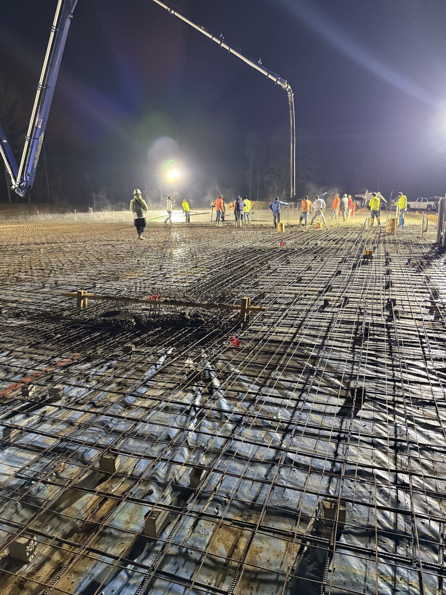 Night concrete slab pour at the Bryant Machine shop site — crew placing concrete over the rebar mat with a pump truck